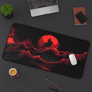 Puede incluir: Alfombrilla de escritorio rectangular negra con una ilustración roja y negra de un jinete a caballo contra un sol rojo, con olas estilizadas. Un ratón blanco está a la derecha. También se ve una taza de café y una planta.