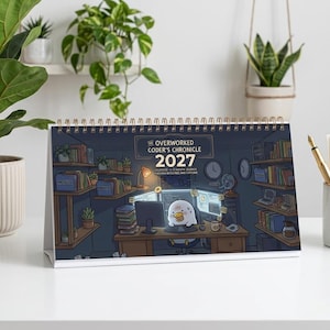May include: A 2027 desk calendar titled The Overworked Coder's Chronicle featuring a cartoon illustration of a duck working at a computer desk surrounded by bookshelves, clocks, and office supplies, bound with a gold-colored metal spiral coil.