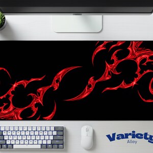 May include: A rectangular desk mat featuring a solid black background with a vibrant, glossy red abstract tribal flame pattern extending across the surface. The design consists of sharp, curved, and interconnected shapes that create a high-contrast visual effect.