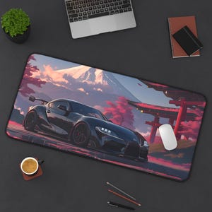 May include: A black sports car with a red and white background. The car is driving past a red Japanese temple gate. The background is a mountain range with a pink and orange sunset.