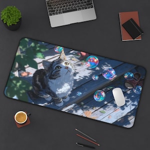 May include: A rectangular desk mat featuring a digital illustration of a tabby cat gazing upwards at colorful bubbles. The cat is sitting on a wooden surface, with a laptop, mouse, and other office supplies visible.