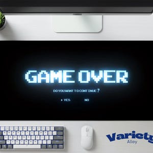 Op de afbeelding: Zwarte rechthoekige bureaumat met de woorden "GAME OVER" in pixelige blauwe letters. Daaronder staat "DO YOU WANT TO CONTINUE?" met de opties "YES" en "NO". Een toetsenbord en muis zijn eronder zichtbaar.