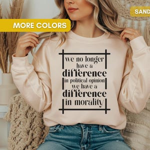 May include: Sand-colored sweatshirt with the text "we no longer have a difference in political opinion we have a difference in morality" in black. The sweatshirt is long-sleeved and has a crew neck.
