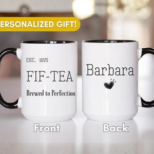 May include: Two white ceramic mugs with black handles and rims. The front mug features the text EST. 1975, FIF-TEA, and Brewed to Perfection. The back mug displays the name Barbara above a small hand-drawn heart icon in black ink.