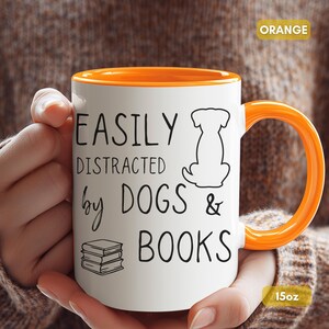 White ceramic mug with a black handle and rim. The mug features the text "EASILY DISTRACTED by DOGS & BOOKS" in black, along with a dog silhouette and stacked books.