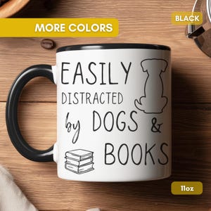 White ceramic mug with a black handle and rim. The mug features the text "EASILY DISTRACTED by DOGS & BOOKS" in black, along with a dog silhouette and stacked books.
