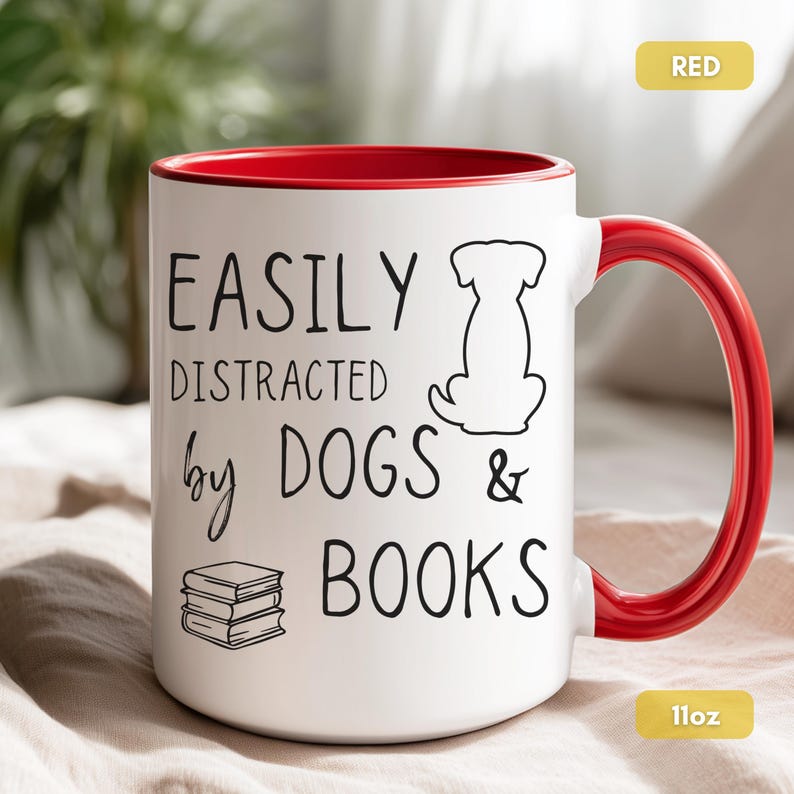 White ceramic mug with a black handle and rim. The mug features the text "EASILY DISTRACTED by DOGS & BOOKS" in black, along with a dog silhouette and stacked books.