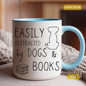 White ceramic mug with a black handle and rim. The mug features the text "EASILY DISTRACTED by DOGS & BOOKS" in black, along with a dog silhouette and stacked books.