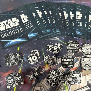 May include: A collection of Star Wars Unlimited trading cards and game tokens. The cards are black with white text that reads "Star Wars Unlimited". Tokens include numbers, "FORCE", "BLAST", and "PLAN".
