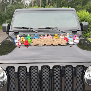 May include: A display of brightly coloured rubber ducks, each with a unique design, arranged on the bonnet of a black vehicle. The ducks vary in size and feature details like hats and accessories.