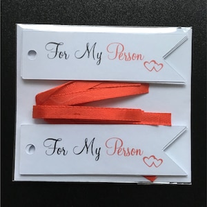 May include: Two white gift tags with red ribbon. Each tag has a hole punched in the top left corner and says "For My Person" in black cursive with two pink hearts.
