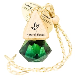 May include: A green glass car air freshener with a wooden top that says "Natural Blends". The air freshener is hanging from a string.