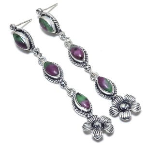 May include: A pair of silver dangle earrings with green and purple gemstones. The earrings feature a flower design at the bottom.
