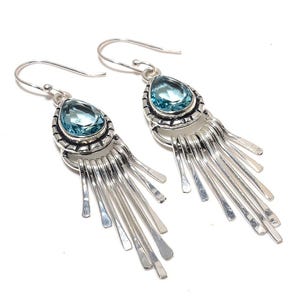 Puede incluir: Pendientes de plata con una piedra preciosa azul en forma de lágrima y un diseño de flecos.