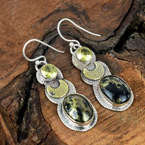May include: A pair of silver dangle earrings with a black and gold stone and a yellow gemstone. The earrings have a crescent moon design.