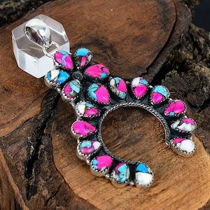 May include: A silver-toned pendant with a crescent shape, adorned with vibrant pink, turquoise, and white gemstones. The pendant has a clear, rectangular bail. The gemstones are set in a detailed, textured metalwork design.