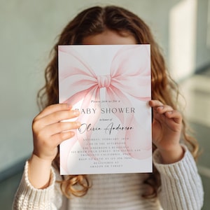 May include: Baby shower invitation with a watercolor pink bow design. The invitation includes the text "Please join us for a BABY SHOWER in honor of Olivia Anderson". Additional details include the date, time, and location.