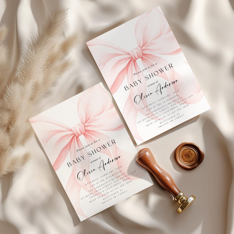 May include: Two baby shower invitations with a watercolor pink bow design. The invitations include the text "Baby Shower" and the name "Olivia Anderson". A wooden stamp and wax seal are also present.