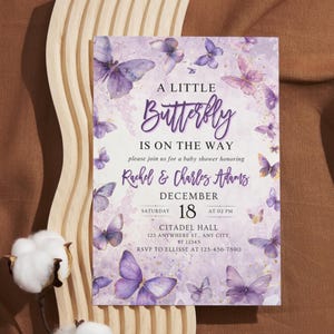 May include: A baby shower invitation with a butterfly theme. The invitation features a purple and white color scheme with butterfly illustrations. The text reads "A Little Butterfly Is On The Way" and includes event details.