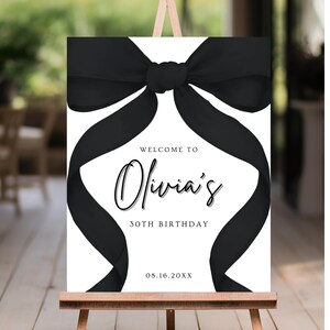 May include: A white welcome sign with a black bow on top. The sign reads "Welcome to Olivia's 30th Birthday 08.16.20XX".