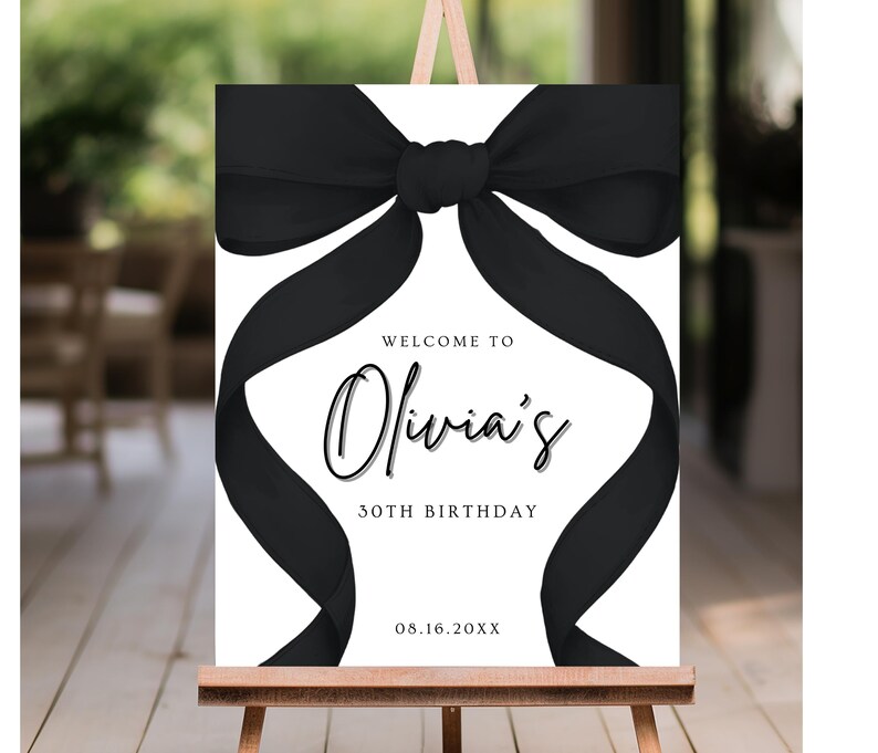 May include: A white welcome sign with a black bow on top. The sign reads "Welcome to Olivia's 30th Birthday 08.16.20XX".