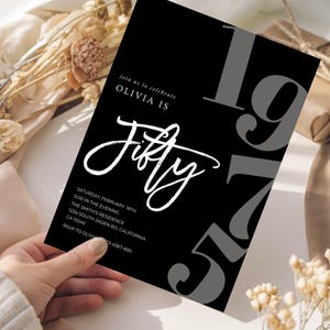 May include: Black invitation card with white script text that reads "Olivia is Fifty." The number "197" is in gray on the right side. Additional text includes the date, time, and location of the event.