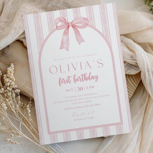 May include: A pink and white striped invitation for Olivia's first birthday. The invitation features a pink bow, an arched frame, and the text "OLIVIA'S first birthday" with the date and time. The invitation also includes the address and RSVP information.