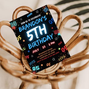 May include: A black and white birthday invitation with colorful accents. The invitation says "Join us to celebrate Brandon's 5th Birthday" with a neon blue "5th" and a date of July 23rd at 2 PM. The invitation also includes the address and RSVP information.