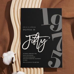 May include: Black birthday invitation with the text "Olivia is Fifty" in white script. The number "1975" is in gray, with event details below. The invitation is on a brown surface with cotton flowers and a wooden accent.