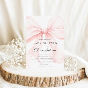 May include: A baby shower invitation featuring a large, watercolor-style pink bow. The invitation includes the text "Baby Shower" and details for Olivia Anderson's shower, including date, time, and location. The invitation is on a white background.