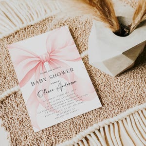May include: A baby shower invitation with a watercolor pink bow design. The invitation includes the text "BABY SHOWER" and details for the event, including the honoree's name, date, time, and location. RSVP information and registry details are also included.