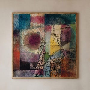 Pode incluir: Impressão de arte abstrata em uma moldura de madeira. A obra de arte apresenta um design geométrico com uma variedade de cores, incluindo azul, vermelho, roxo e amarelo. A impressão tem uma aparência texturizada e é exibida em uma parede de cor clara.