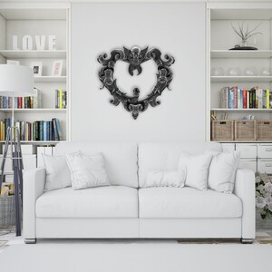 Puede incluir: Un sofá blanco con almohadas blancas en una sala de estar con estanterías blancas empotradas. Las estanterías están decoradas con libros, un jarrón con ramas y cestas de mimbre. Una decoración de pared en forma de corazón negro y plateado cuelga de la pared sobre el sofá.