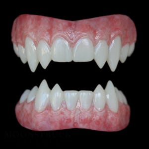 May include: A set of upper and lower dental prosthetics featuring pointed, elongated canine teeth. The gums are a textured, mottled pink colour, and the teeth are white with a glossy finish. The text MOONSTRUCK EFFECTS is visible at the bottom.