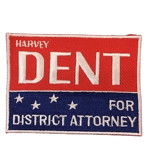 Puede incluir: Parche rectangular con una sección superior roja y una sección inferior azul. La palabra "DENT" está en letras blancas grandes. Encima está "HARVEY" y debajo "FOR DISTRICT ATTORNEY" con estrellas blancas.