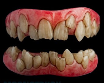 Peut inclure: Un ensemble de prothèses dentaires supérieures et inférieures avec une base de gencives roses et des dents décolorées, mal alignées et pointues. L'appareil dentaire présente un aspect usé avec un espacement irrégulier et des bords tranchants.