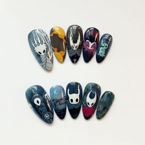 May include: A set of ten almond-shaped false nails, each hand-painted with a different design. The designs feature characters and imagery from the video game Hollow Knight, in shades of blue, white, yellow, and red. The nails are arranged on a white surface.