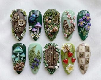 Può includere: Una collezione di dieci nail art dal design intricato. Ogni unghia presenta un design unico ispirato alla natura, tra cui funghi, insetti, fiori e una porta delle fate in miniatura. La tavolozza dei colori comprende verdi, marroni e pastelli, con texture dettagliate.