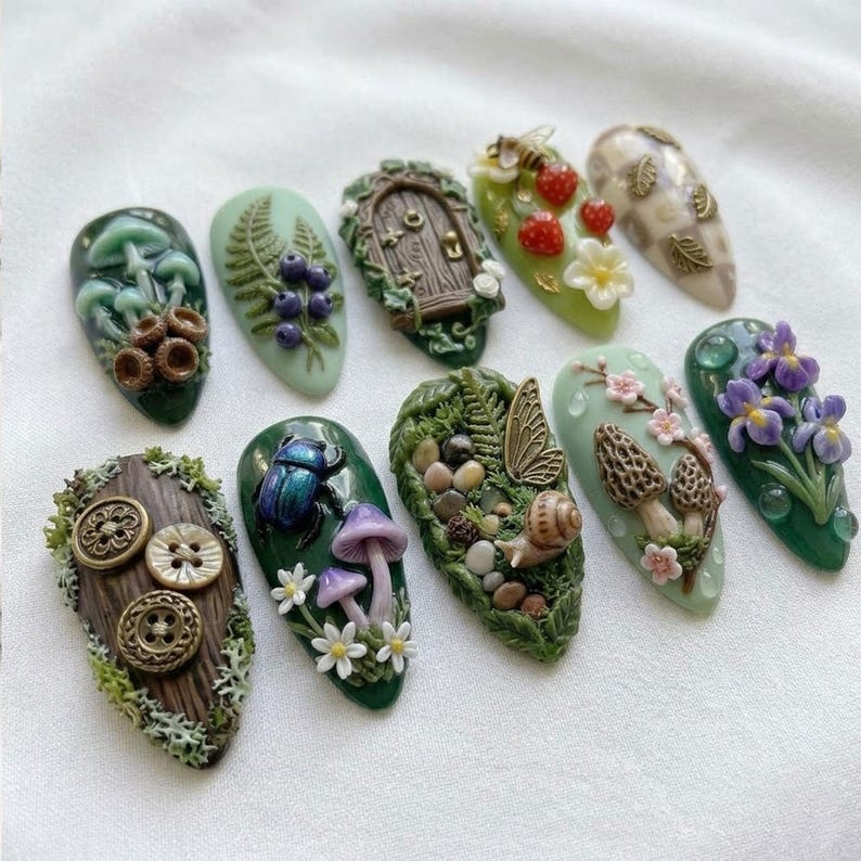 May include: A collection of ten uniquely designed nail art sets. Each nail features a different nature-inspired design, including mushrooms, berries, a fairy door, and a beetle. The nails are painted in various shades of green, brown, and purple.