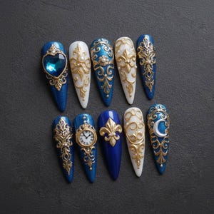 May include: A set of ten long, pointed artificial nails. The nails feature a variety of designs, including gold filigree, a heart-shaped jewel, a clock face, and a fleur-de-lis, set against a blue and white background.