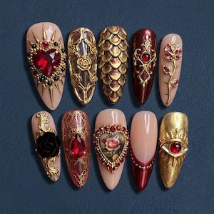 May include: A collection of ten artificial nails with diverse designs. The nails showcase gold and red adornments, including hearts, roses, and intricate patterns. Some nails have a nude base, while others are painted in shades of red and gold.