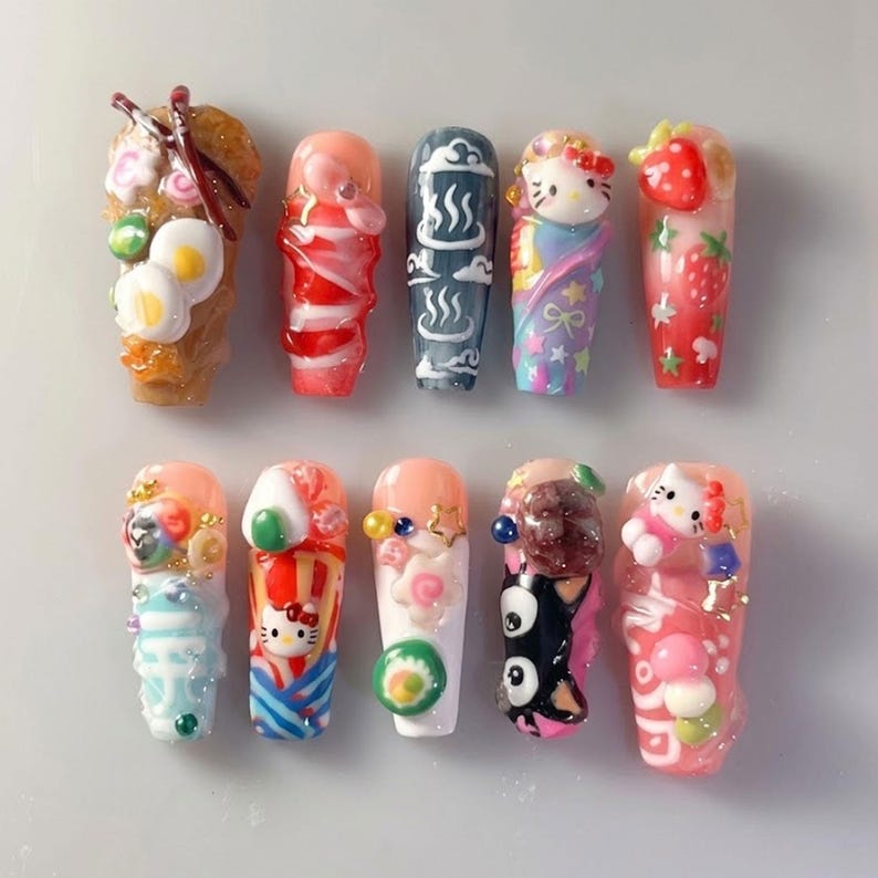 May include: A collection of ten uniquely designed nail art sets. Each nail features a different design, including food-themed elements like sushi and eggs, and character designs such as Hello Kitty. The nails are in various colors, including pink, red, and blue.