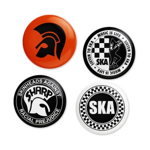 Op de afbeelding: Vier ronde zwart-witte knoppen met een schaakbordpatroon en het woord "SKA" in witte letters. Eén knop heeft een silhouet van een dansende persoon met de tekst "LISTEN TO SKA MUSIC IS LIFE" rond de rand. Een andere knop heeft een zwart-wit silhouet van een mohawk met de tekst "SKINHEADS AGAINST RACIAL PREJUDICE SHARP" rond de rand.