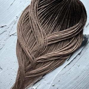 Op de afbeelding: Een set lange, bruine ombre synthetische dreadlocks. De dreadlocks zijn in een losse vlecht geordend en hebben een lichtbruine kleur bij de wortels die geleidelijk overgaat in een donkerdere bruine kleur aan de uiteinden.