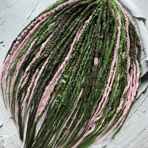 May include: A set of synthetic dreadlocks in shades of green and pink. The dreadlocks are long and straight, with a variety of textures and styles.
