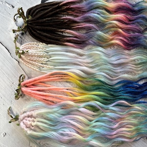 May include: Four sets of colourful synthetic dreadlocks, each with a different colour gradient. The dreadlocks are arranged in a row, with the darkest set at the top and the lightest set at the bottom. The colours include brown, white, pink, and light blue.