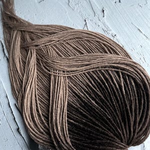 May include: A bundle of brown and black ombre synthetic dreadlocks. The dreadlocks are arranged in a circular pattern.