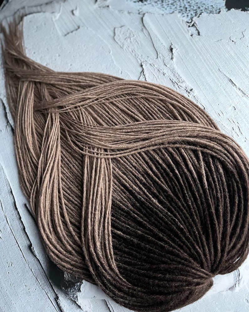 May include: A bundle of brown and black ombre synthetic dreadlocks. The dreadlocks are arranged in a circular pattern.