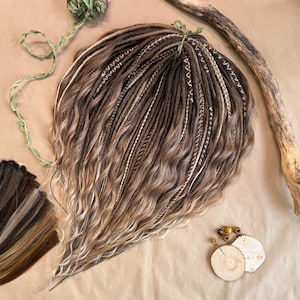 May include: A set of brown and blonde synthetic dreadlocks with white accents. The dreadlocks are wavy and have a natural look.