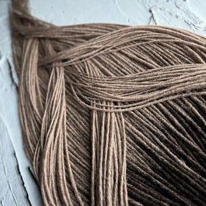 May include: A close-up of a bundle of brown and dark brown synthetic dreadlocks. The dreadlocks are arranged in a criss-cross pattern.
